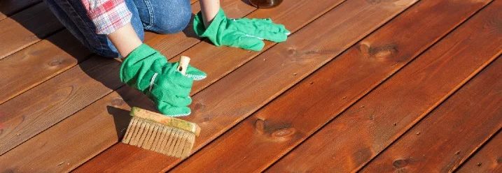 Person streicht Holzdielen mit Pinsel